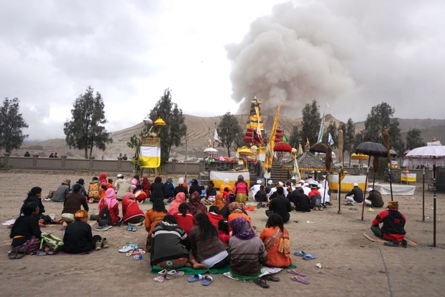 Warga bersembahyang dalam ritual Yadnya Kasada di Pura Poten Luhur Bromo di kawasan Gunung Bromo, Jatim, dengan latar gunung Bromo yang sedang erupsi. Foto : Luh De Suriyani