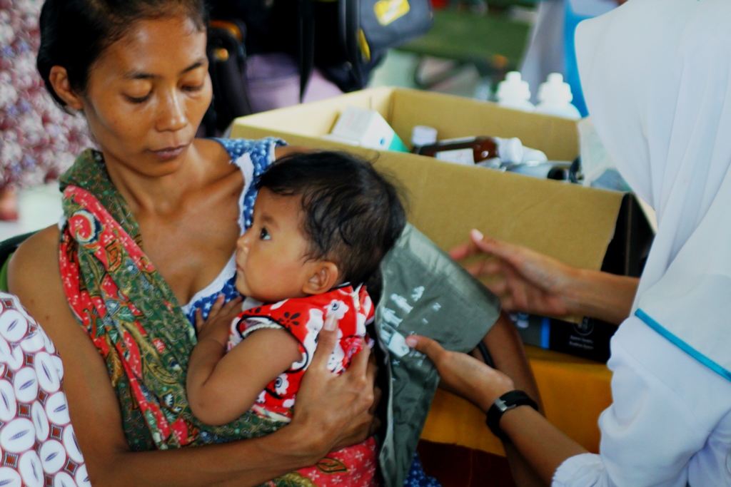 Seorang korban banjir bandang Sungai Cimanuk, Garut, Jabar menggendong anaknya sambil diperiksa kesehatannya di pos pengungsian pada Jumat (23/09/2016). Foto : Donny Iqbal
