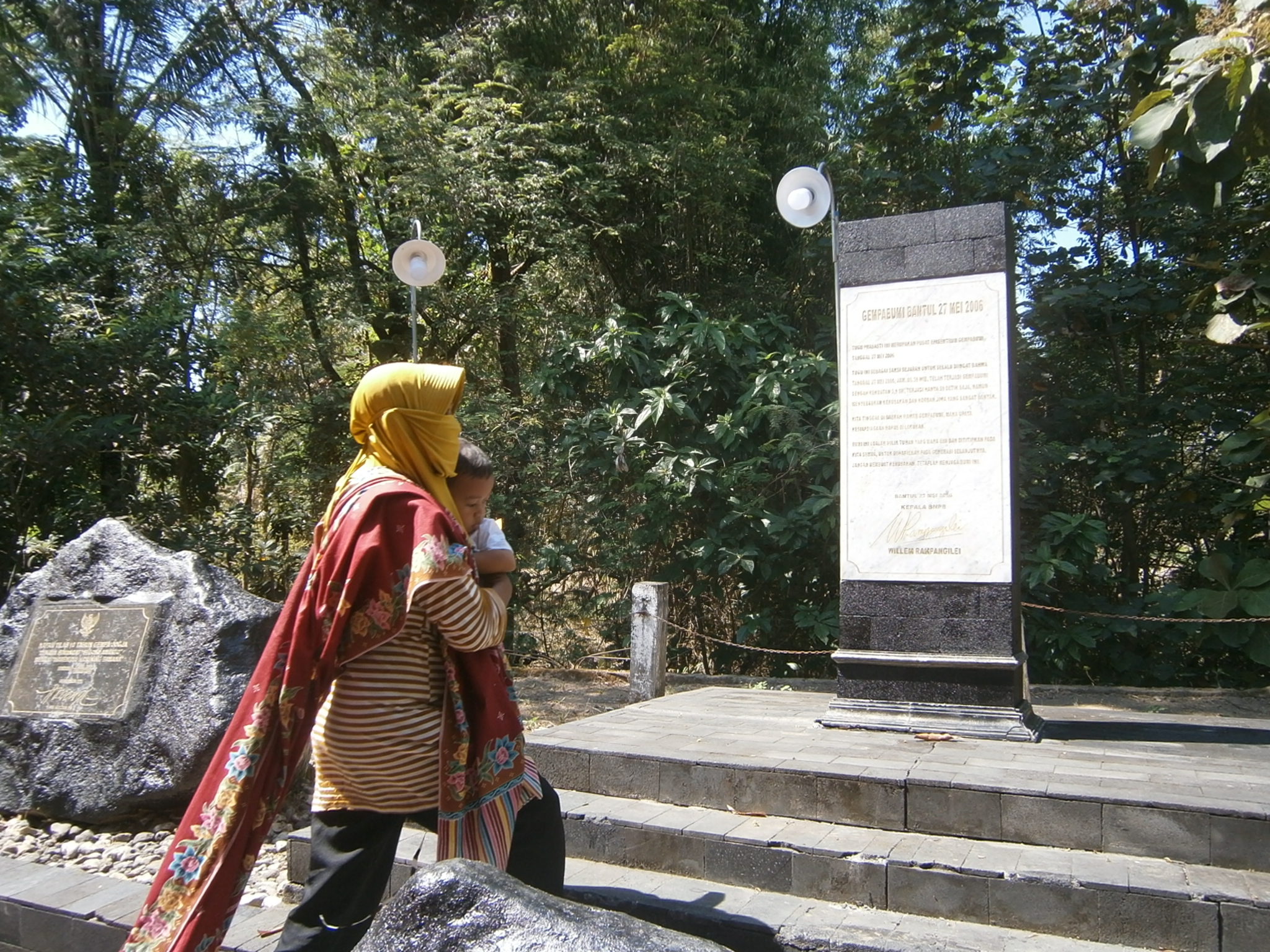 Wartiyem menggendong cucu di tugu prasasti episentrum gempa Bantul. Foto: Nuswantoro/ Mongabay Indonesia