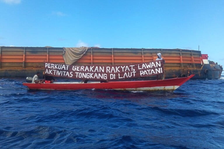 Peserta aksi bentangkan spanduk di dekat tongkang yang mengangkut ore nikel . Foto Zulkadri Husen