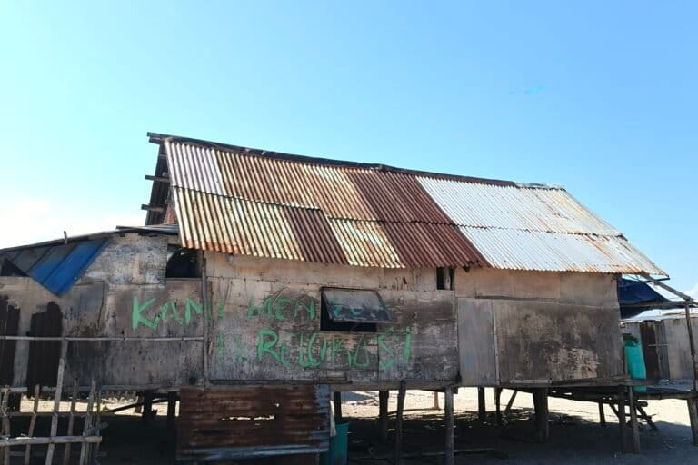 Tulisan “Kami Menolak Direlokasi” terpampang di dinding rumah salah seorang warga. Mereka menolak perampasan ruang hidup mereka. Foto: Mario Sara/ Mongabay Indonesia