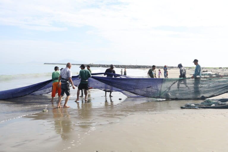Sekelompok laki-laki yang terdiri atas 7 orang menarik pukat hingga ke bibir pantai Gampong Jawa. Aktivitas ini sempat terhenti selama hampir sebulan karena banyaknya timbulan sampah yang terbawa arus angin musim barat. Foto: Nurul Hasanah/Mongabay Indonesia